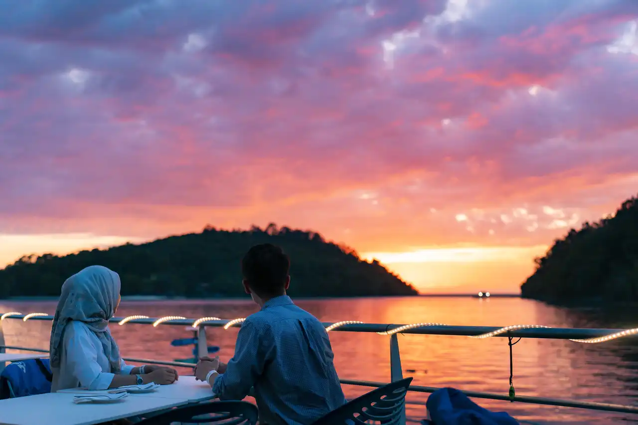 Couple enjoying a sunset dinner on a boat with scenic views of the island and sea