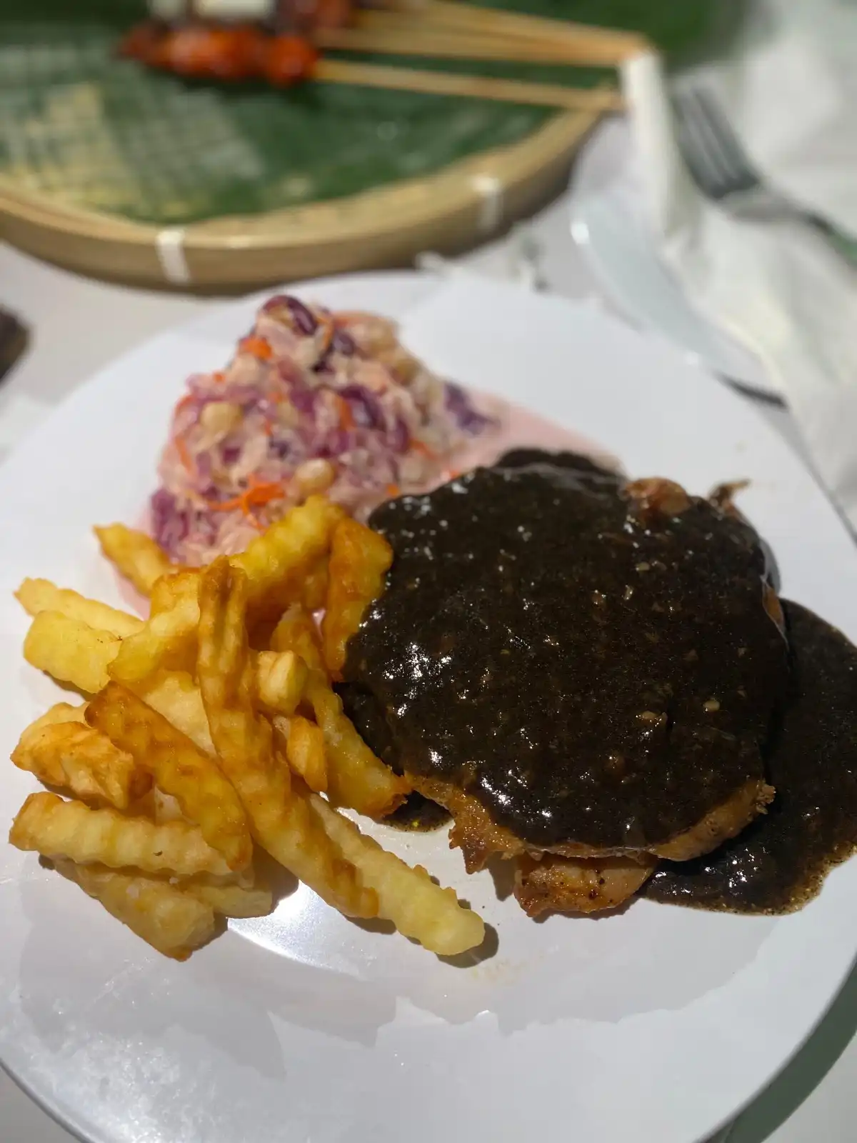 Plate of chicken chop with black pepper sauce, fries, and coleslaw on a white plate.