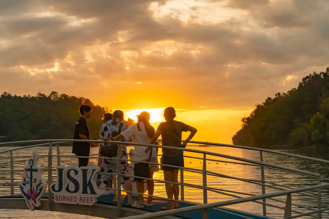 Group of people enjoying a sunset from a boat deck near Borneo Reef.
