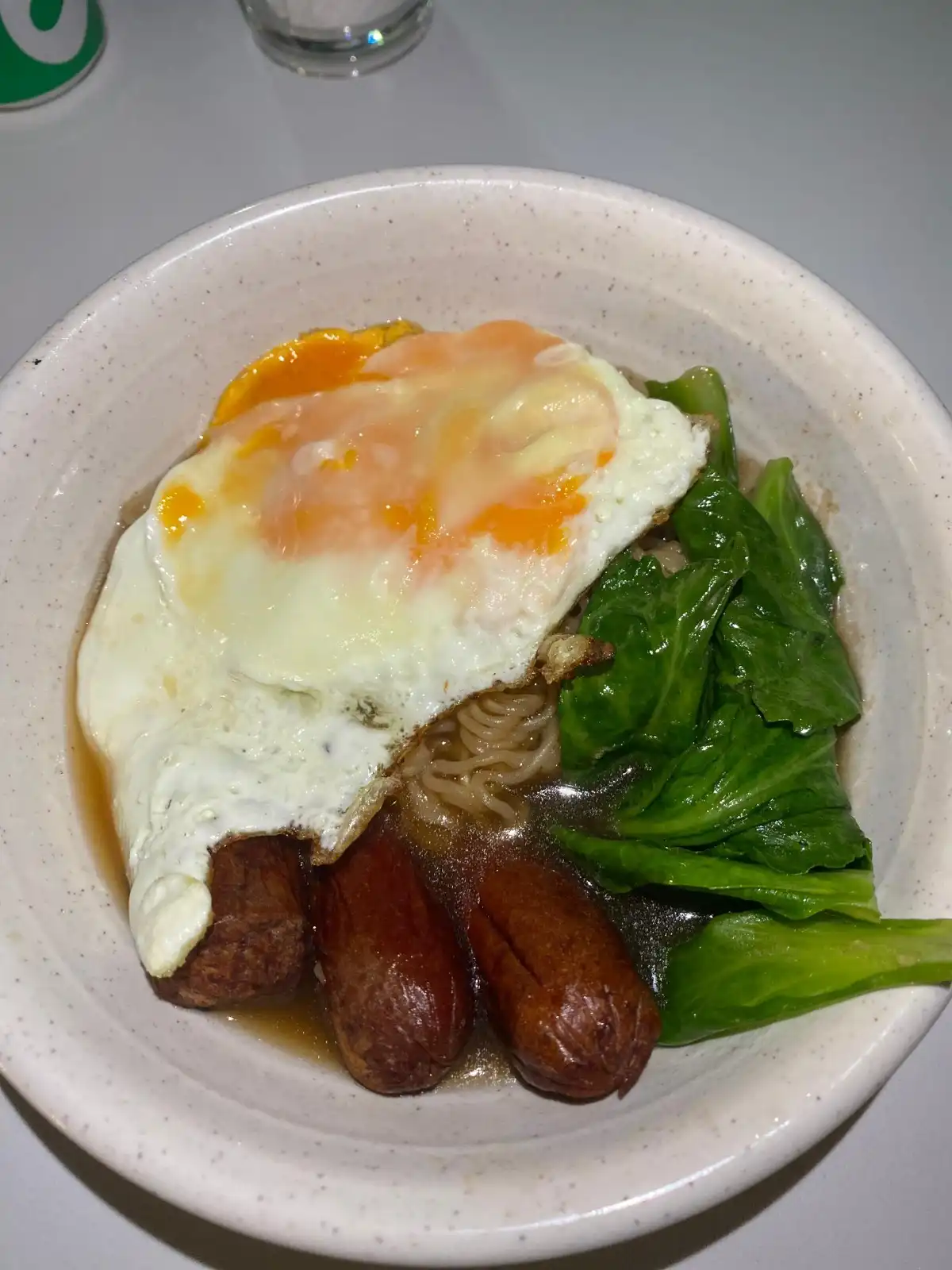 Bowl of noodle soup with fried egg, sausages, and bok choy.