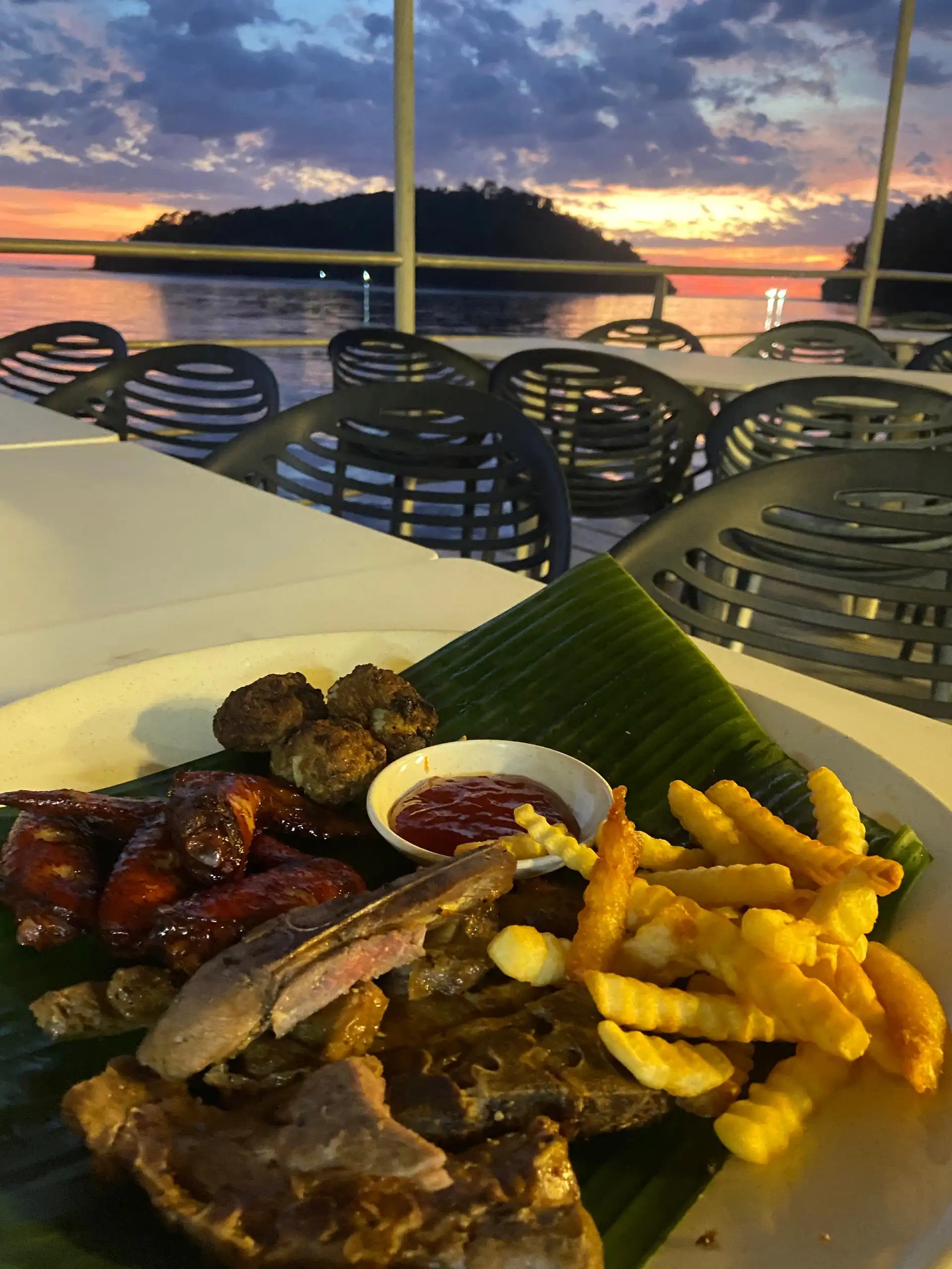 Sunset view over water from a restaurant with a plate of mixed grilled meats and fries on the table.