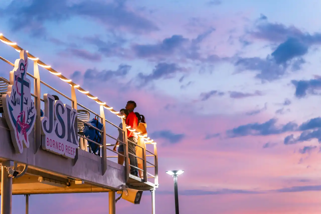 People on a viewing platform at dusk, overlooking the Borneo Reef, with vibrant sunset skies.