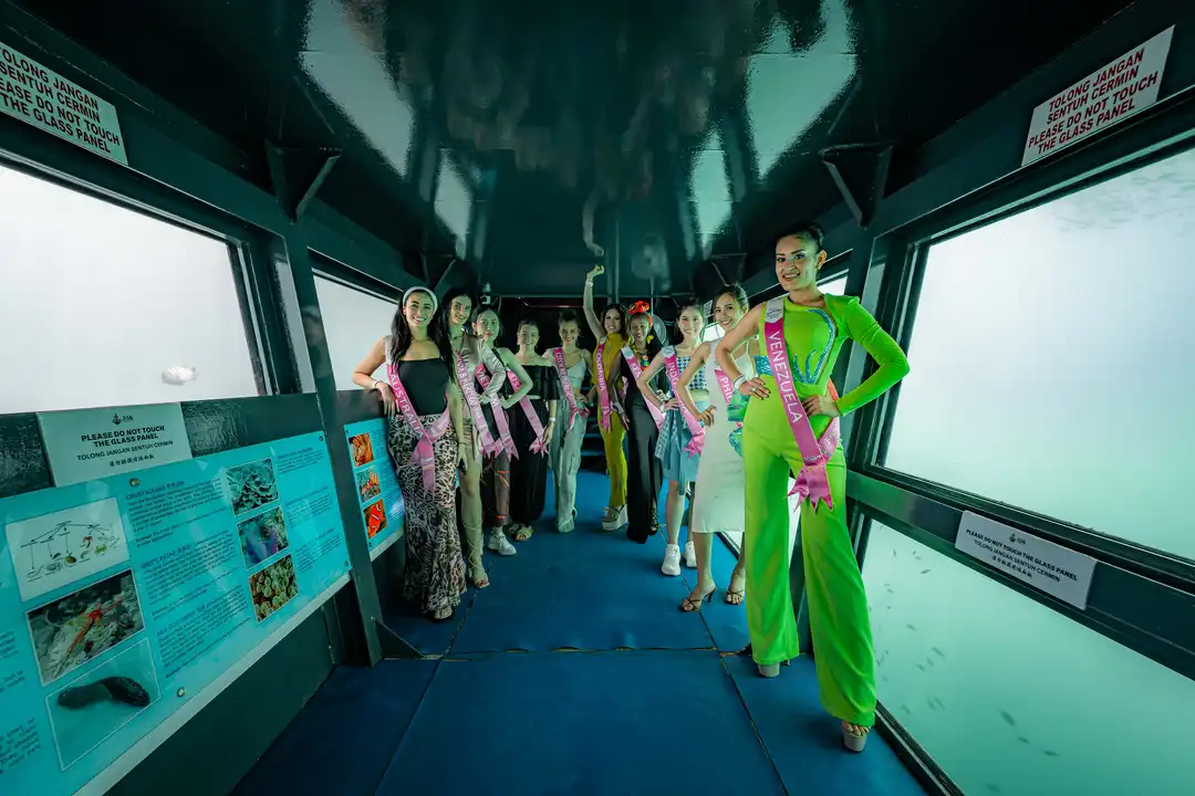 Group of beauty pageant contestants in sashes inside an underwater observatory in Kota Kinabalu.